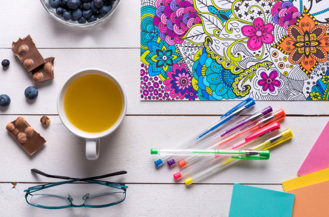 Flat-lay of an adult coloring book with colored pencils and a cup of tea, illustrating creative relaxation and self-care.