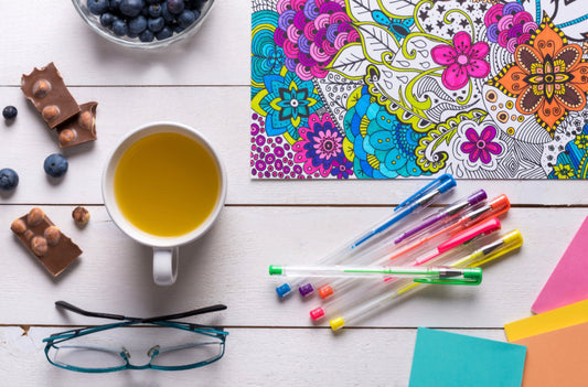 Flat-lay of an adult coloring book with colored pencils and a cup of tea, illustrating creative relaxation and self-care.